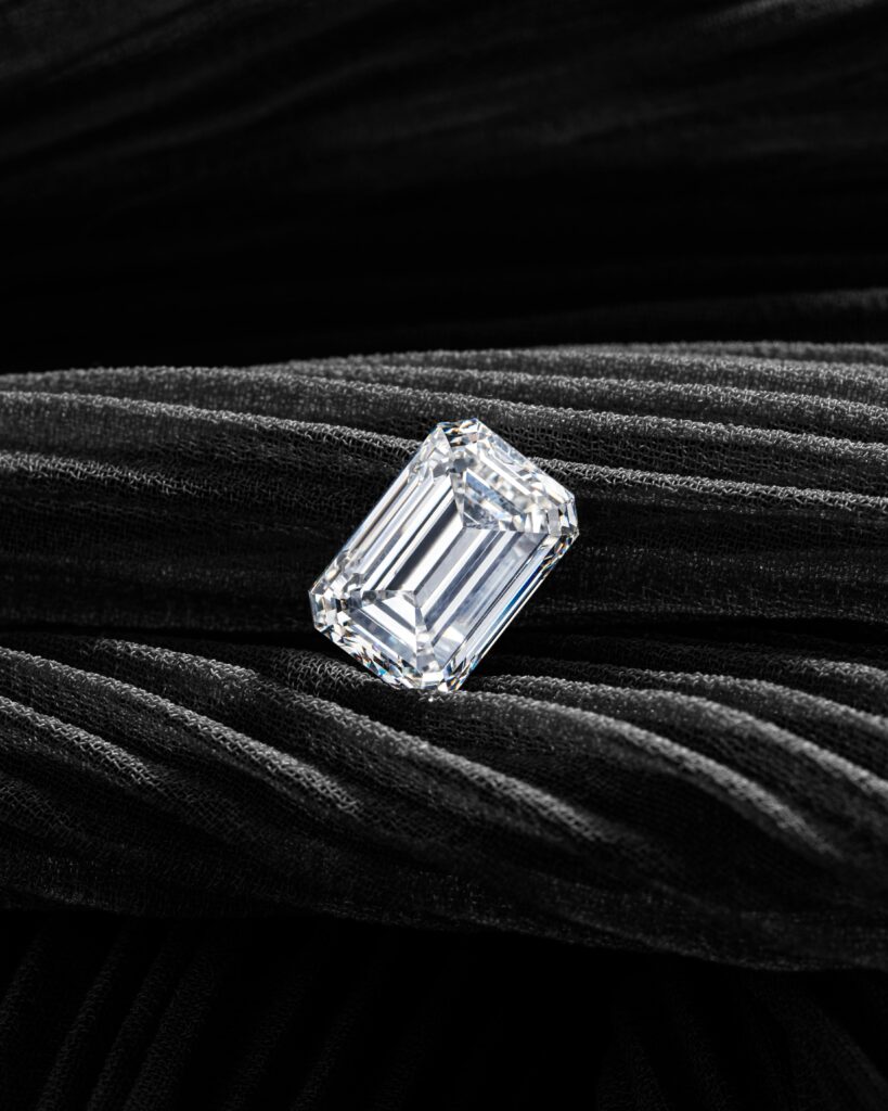 A radiant emerald-cut diamond showcased on a textured black velvet background, exuding elegance and luxury.
